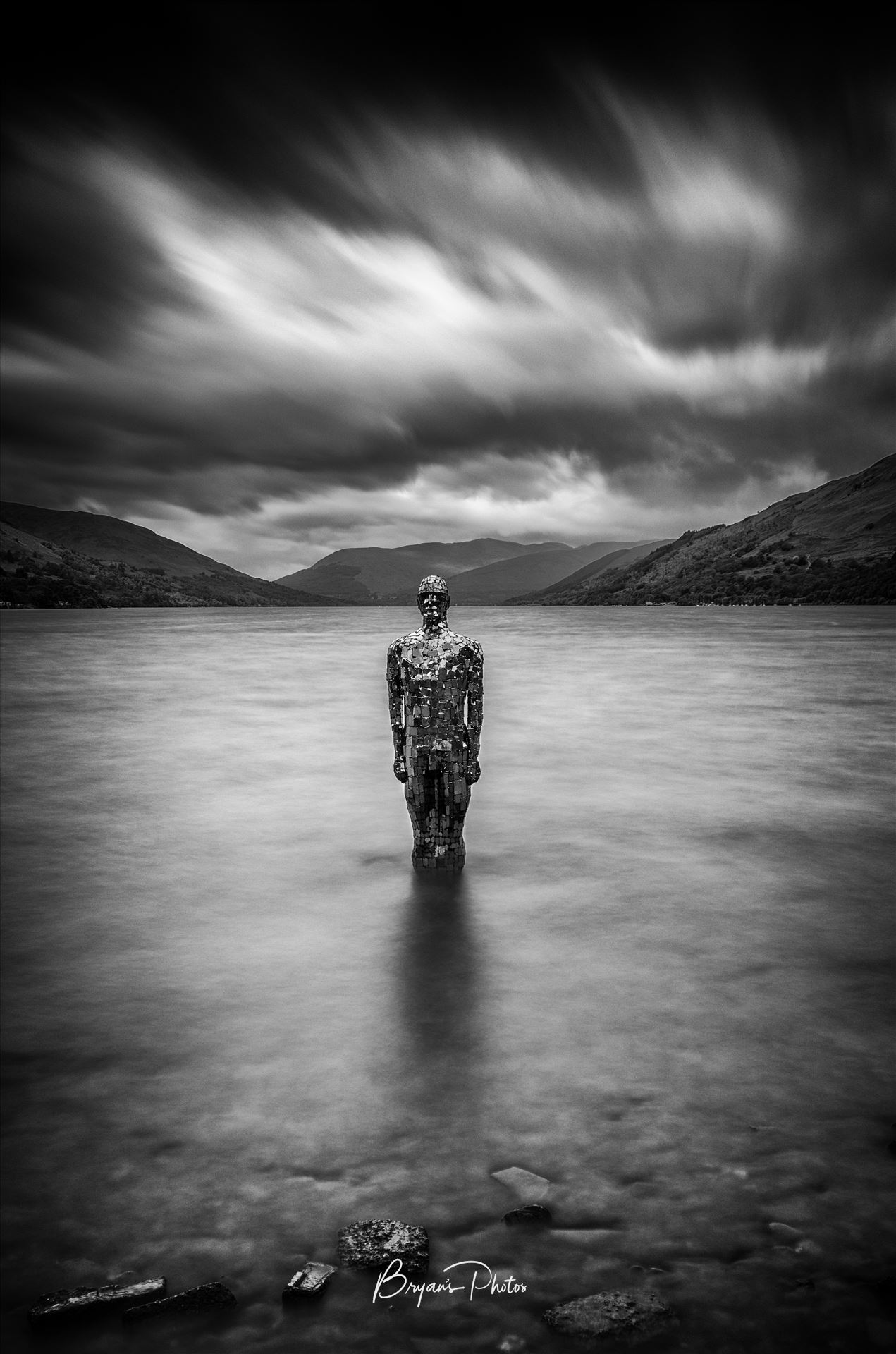 Still at St Fillans - A long exposure photograph of the still mirror man sculpture taken from St Fillans at Loch Earn. by Bryans Photos