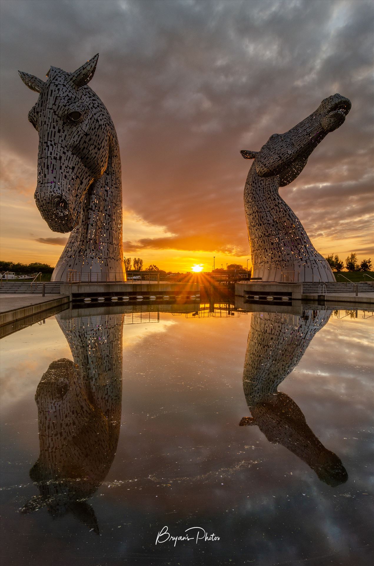 Sunset at the Kelpies - A photograph of the Kelpies taken as the sun sets in between them. by Bryans Photos