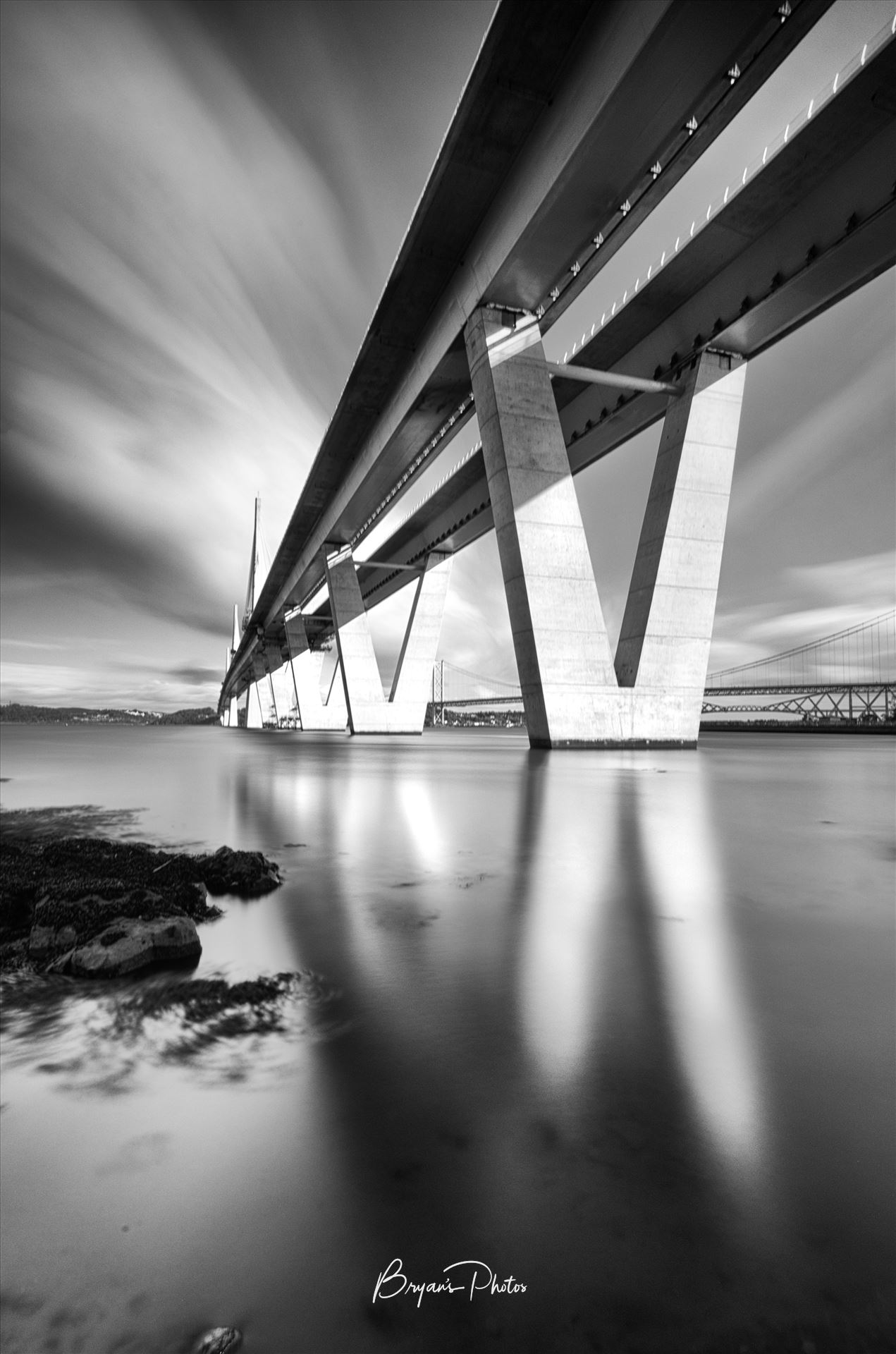 The Crossing Portrait - A black and white long exposure photograph of the Queensferry Crossing taken from the south bank of the river Forth at high tide. by Bryans Photos