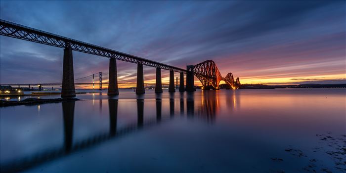 A panoramic photograph of the Forth Rail Bridge taken at sunset from the banks of the river Forth at South Queensferry.