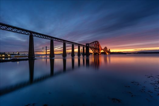 A photograph of the Forth Rail Bridge taken at sunset from the banks of the river Forth at South Queensferry.