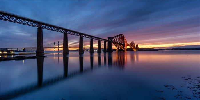 A panoramic photograph of the Forth Rail Bridge taken at sunset from the banks of the river Forth at South Queensferry.